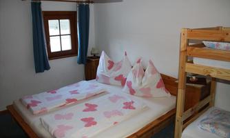 A cozy bedroom with a double bed and a bunk bed. The bedding is decorated with colorful butterflies, and the room has a large window with blue curtains.
