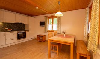 A bright and cozy kitchen with a dining table and wooden paneling. The walls are painted in soft colors, and there is a small television on the wall.