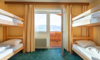 A bright sleeping area with two bunk beds and large windows. The view overlooks a balcony with a view of the mountains.