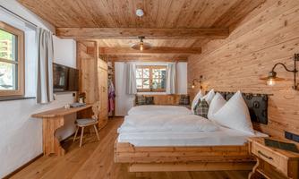 A cozy room with wooden decor and two beds. Large windows let in plenty of light and create a warm atmosphere.