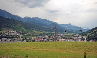 A picturesque landscape with green hills and mountains in the background. In the foreground, there is a cable car that passes over the city.
