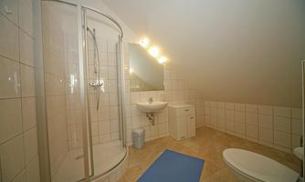 A modern bathroom with a shower, sink, and toilet. Bright tiles and a blue bath mat create a welcoming atmosphere.