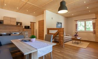 A bright and modern apartment with wooden details. The room features a dining area, a cozy couch, and large windows that provide plenty of light.