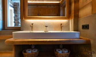 A modern bathroom with an elegant sink and wood details. In the background, wooden cabinets and a warmly lit wall can be seen.