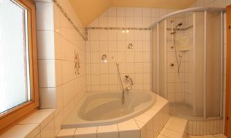 A bathroom with a round bathtub and a shower cabin. The walls are tiled and a window provides natural light.