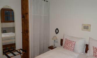 A cozy bedroom with two beds and white bed covers. Next to the beds is a small nightstand, and a mirror is mounted on the wall.