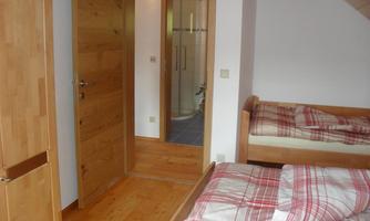 A cozy bedroom with two beds and a wooden floor. In the background, a door to a bathroom can be seen.