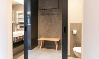 A modern bathroom with a wooden bench and a clear view of the sanitary facilities. The walls are in neutral tones, which creates an elegant atmosphere.