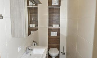 A modern bathroom with a sink and a toilet. The walls are light, and the floor has a dark wood design.