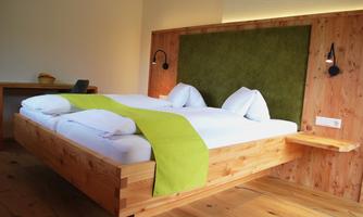 A modern bedroom with a wooden bed and green wall paneling. The cozy atmosphere is enhanced by the bright light and the simple design.