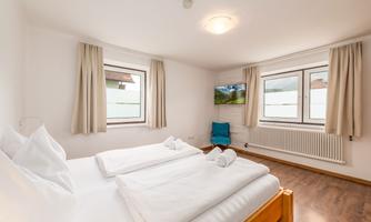 A bright bedroom with two single beds and white bed linen. Large windows let in plenty of daylight and offer a view outside.