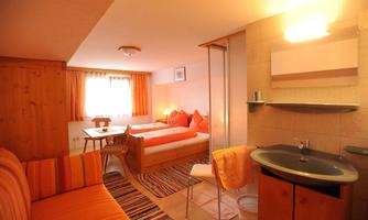 A cozy room with a double bed and colorful decoration. There is a living area with a sofa and a table.