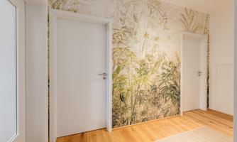 A bright hallway with two white doors and a wallpaper with a plant pattern. The floor is made of wood and gives the room a warm atmosphere.