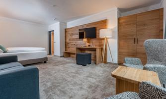 A modern hotel room with a comfortable bed, a couch, and a television. The decor is stylish and warm, featuring wood elements and neutral colors.