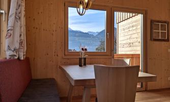 A bright room with wooden paneling and a table. Through the window, one looks out at a beautiful mountain landscape.