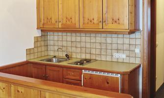 A small kitchen unit made of wood with cabinets and a sink. The room has a warm, cozy atmosphere.