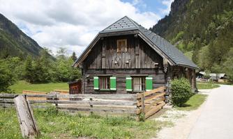 A traditional wooden house with green shutters in a picturesque mountain landscape. Surrounded by meadows and a clear sky.