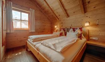 A cozy bedroom with wood paneling and two beds. Large windows let in plenty of daylight.