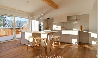 A modern kitchen with a light wood floor and a large window. The designed interior offers plenty of natural light and an inviting atmosphere.