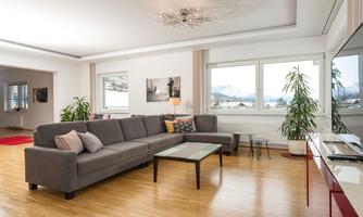 A modern living room with a gray couch and a coffee table.  
Large windows offer a view of the mountains and plenty of daylight.