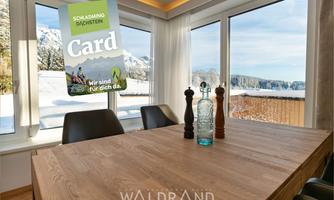 A bright dining area with a wooden table and elegant chairs. Through the windows, a snowy landscape with mountains can be seen.