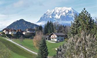 A picturesque landscape with snow-capped mountains in the background. Below lie idyllic houses surrounded by trees and meadows.