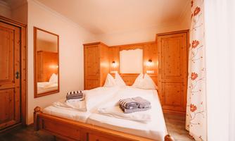 A cozy bedroom with a double bed and wood paneling. There is a large mirror and decorative curtains.
