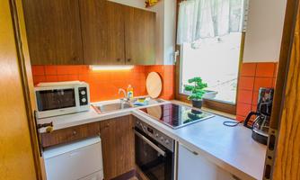 A small, modern kitchen with wooden furniture and orange tiles. The kitchen is well equipped with a stove, a refrigerator, and a microwave.