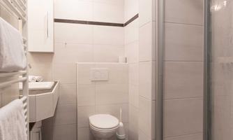 A modern bathroom with a shower, a sink, and a toilet. The space is bright and well-designed, with white tiles and a dark floor.