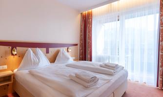 A cozy bedroom with two single beds and fresh towels. Large windows let in plenty of light and provide a view outside.
