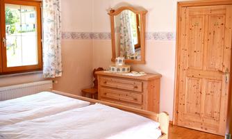 A bright bedroom with a double bed and a wooden wardrobe. Plenty of daylight comes in through the window.