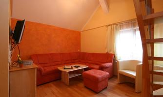 A cozy living room with a red sofa and a small table. The walls are painted orange and there is a lot of daylight coming through the window.