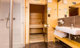 A modern bathroom with a shower and a sauna. The walls are made of wood, and there is a sink with towels.