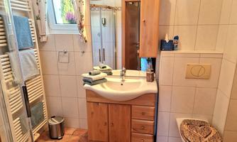 A modern bathroom with a wooden sink, towels, and a shower. The walls are tiled, and there is pleasant lighting.