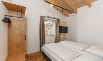 A modern bedroom with a wooden ceiling and minimalist furnishings. There is a window, a TV, and a clothes rack.