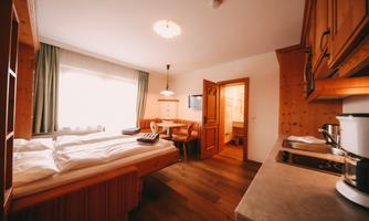 A cozy room with a double bed and a small dining area. The warm wooden design and the window create an inviting atmosphere.