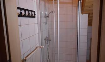 A small bathroom with a shower cabin and white tiles. Some hooks for towels hang on the wall.