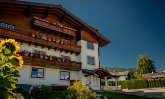 A picturesque house in Alpine style with flower balconies. Surrounded by green spaces and a clear blue sky.