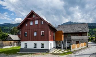 A modern building with red wood cladding and a mixed architecture. Surrounded by a green landscape and mountains in the background.