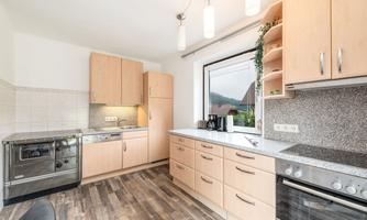 A modern kitchen with bright wooden cabinets and gray countertops. It is well-lit and includes modern kitchen appliances.