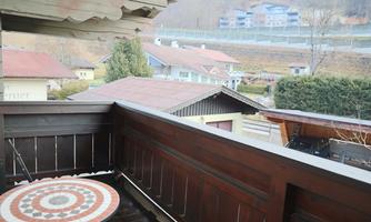 A balcony with a round table and a view of small houses and the surrounding landscape. The atmosphere is peaceful and rural.