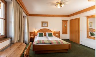 A cozy room with a double bed and wooden decor. The walls are light and the windows provide plenty of daylight.