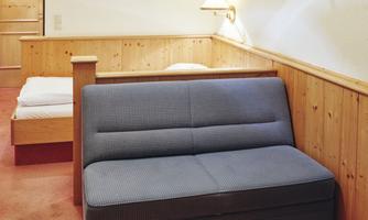 A cozy room with a blue sofa and a double bed in the background. The walls are made of wood, creating a warm atmosphere.