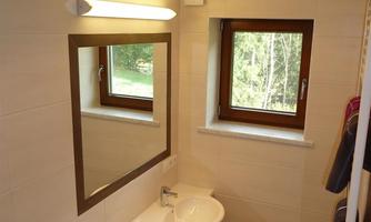 A modern bathroom with two sinks and a large mirror. The light is bright and there is a window with a view of nature.