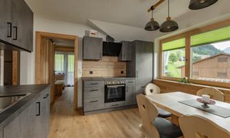 A modern kitchen with wood and gray tones. The space is bright and friendly, with large windows and a dining table.