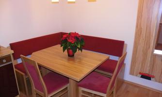 A cozy dining area with a wooden table and a red seating corner. On the table, there is a pot with a plant.