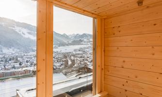 A cozy balcony with wooden cladding and a view of the mountains. In the foreground, there is an open fireplace.