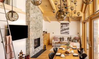 A modern living room with high ceilings and a cozy atmosphere. The space is furnished with a wood stove, a dining table, and stylish light fixtures.
