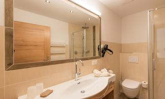 A modern bathroom with a large mirror and a shower cabin. The decor is in neutral colors and creates a bright, inviting atmosphere.