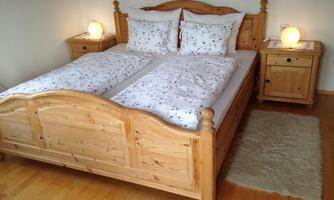 A cozy bedroom with a large, bright wooden double bed. Next to the bed, there are two nightstands with lamp-like lights.